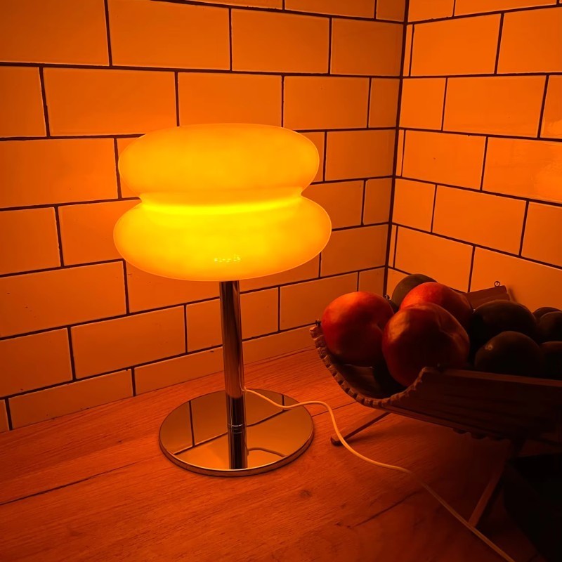 Lampe de table Dimoree en verre soufflé orange en forme de macaron avec pied chromé brillant sur un comptoir en bois