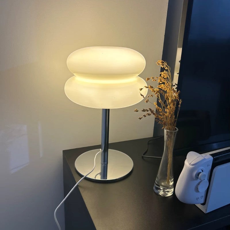 Lampe de table Dimoree en verre soufflé blanc avec pied chromé diffusant une lumière douce sur un meuble noir