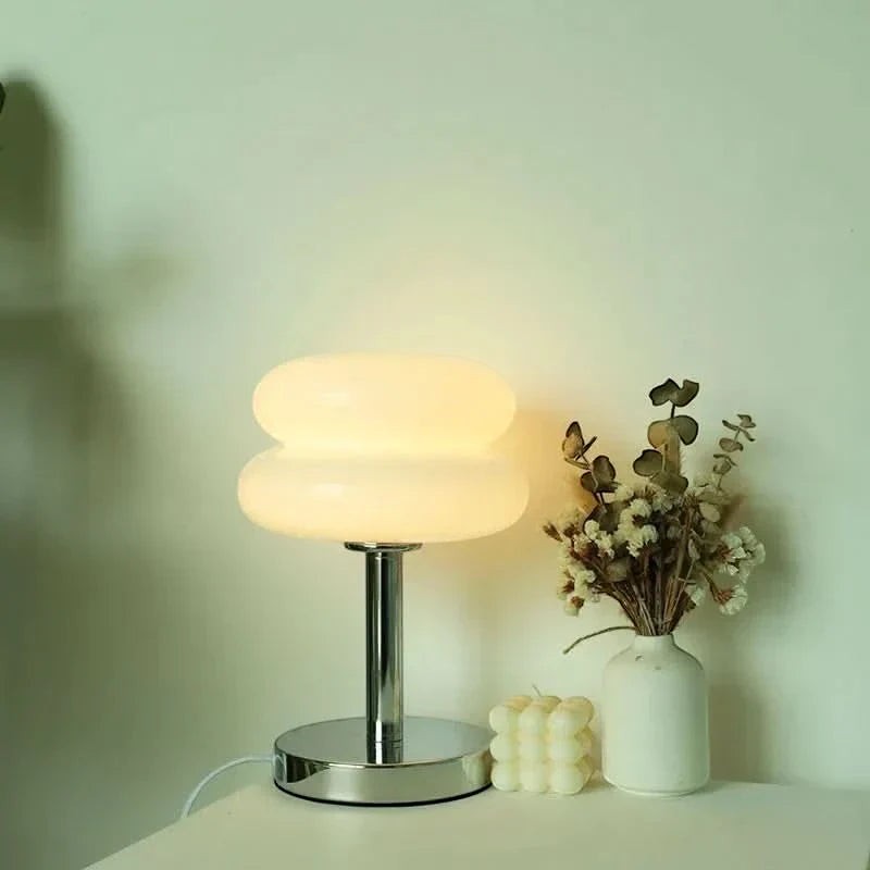 Lampe de table Dimoree en verre soufflé blanc forme macaron avec pied chromé sur une table avec fleurs séchées