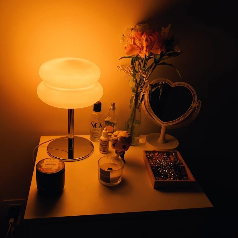 Lampe de table Dimoree en verre soufflé diffusant une lumière chaude et douce sur une table de chevet décorée